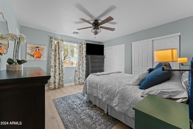 bedroom with ceiling fan, light wood-type flooring, and multiple closets