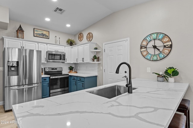 kitchen with white cabinetry, stainless steel appliances, light stone counters, blue cabinets, and kitchen peninsula