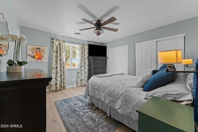 bedroom featuring ceiling fan, light wood-type flooring, and multiple closets