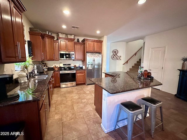 kitchen with appliances with stainless steel finishes, dark stone counters, a kitchen breakfast bar, and sink