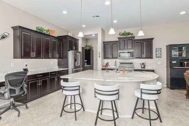 kitchen featuring decorative light fixtures, stainless steel appliances, light tile floors, light stone counters, and a breakfast bar area