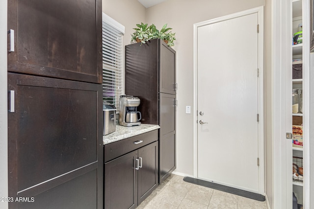 kitchen featuring light tile floors, light stone countertops, and dark brown cabinets