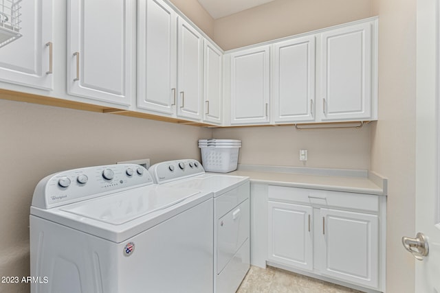 clothes washing area featuring light tile floors, cabinets, and washer and clothes dryer