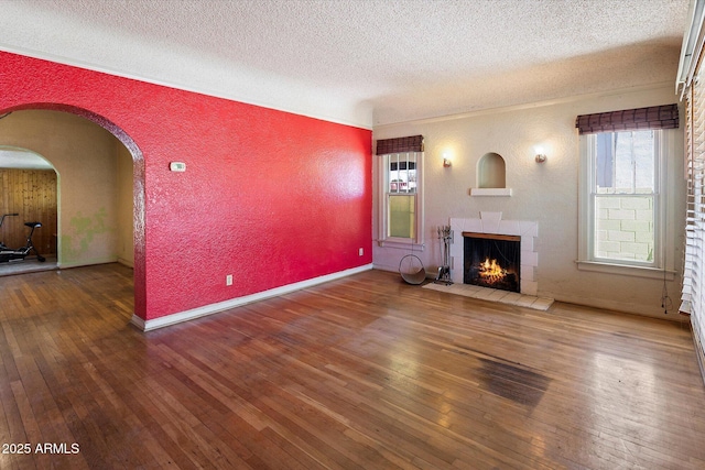 2230 N 12th St Rear, Rear, Phoenix, AZ 85006 - unfurnished living room with a textured ceiling, a textured wall, hardwood / wood-style floors, a lit fireplace, and arched walkways