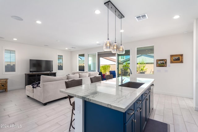 kitchen with blue cabinets, pendant lighting, an island with sink, sink, and light wood-type flooring