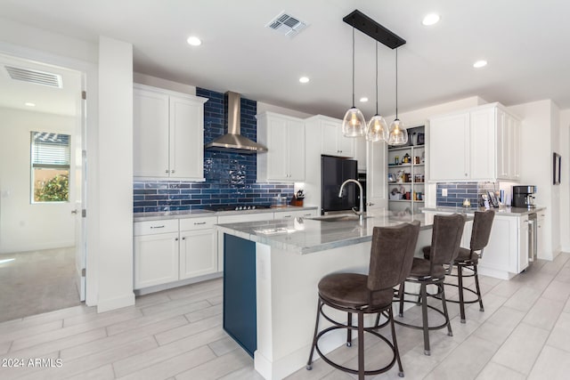 kitchen with black appliances, wall chimney range hood, an island with sink, and white cabinets