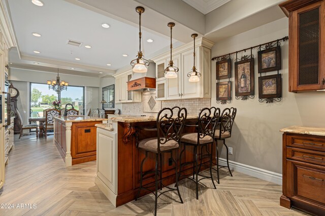 kitchen featuring pendant lighting, a notable chandelier, a kitchen breakfast bar, a center island, and light stone countertops