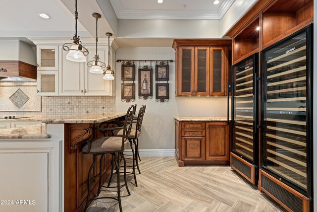 kitchen featuring wine cooler, a kitchen breakfast bar, hanging light fixtures, ornamental molding, and light stone counters