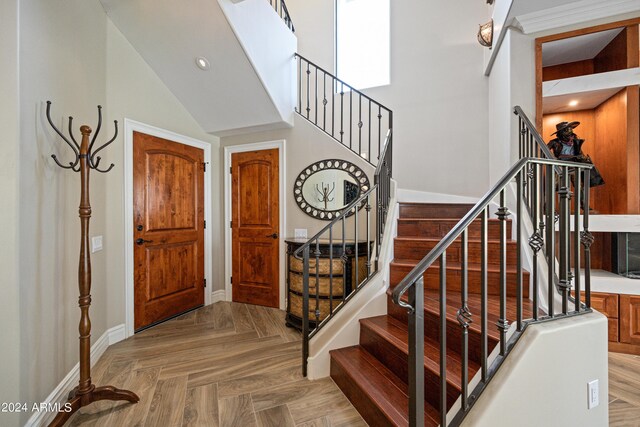 entrance foyer with ornamental molding, vaulted ceiling, and light parquet floors