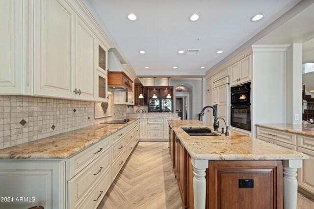 kitchen featuring black appliances, light stone counters, premium range hood, an island with sink, and sink