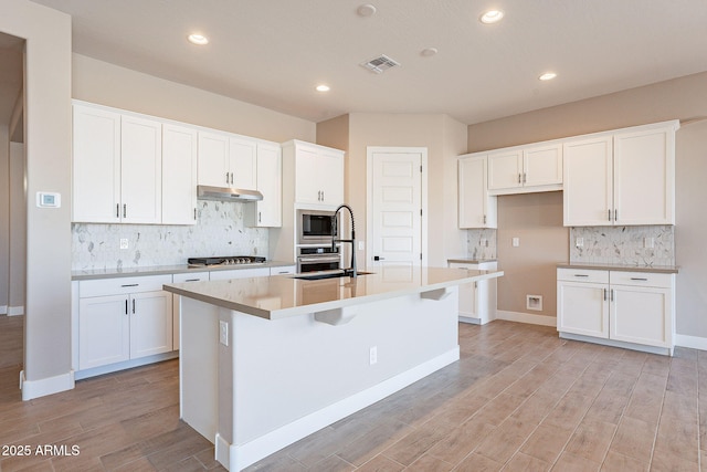 kitchen with stainless steel appliances, light wood-type flooring, a center island with sink, and white cabinets