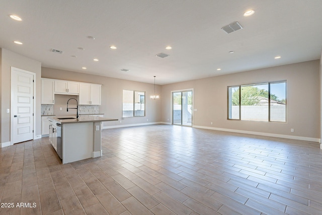 kitchen with sink, white cabinets, backsplash, a notable chandelier, and a center island with sink