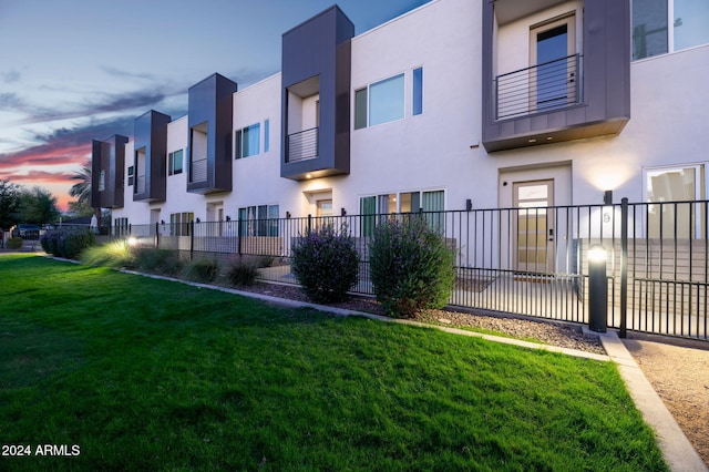 property exterior at dusk featuring a yard and a balcony