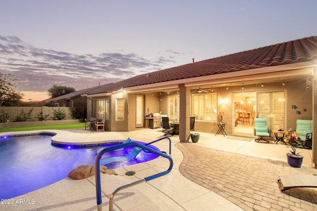 pool at dusk featuring ceiling fan and a patio area