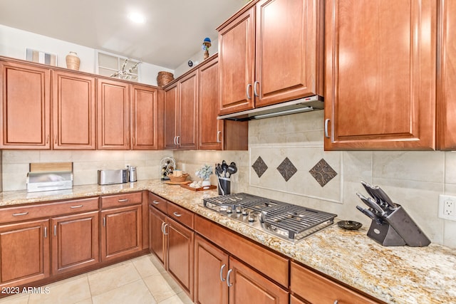 kitchen featuring decorative backsplash, stainless steel gas stovetop, light stone counters, and light tile patterned floors