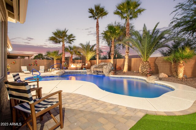 pool at dusk with pool water feature and a patio area