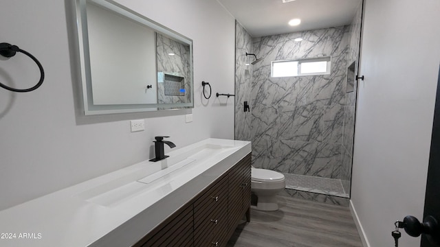 bathroom with a tile shower, vanity, hardwood / wood-style flooring, and toilet