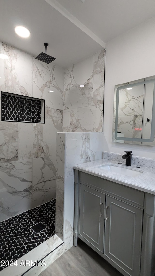 bathroom with a tile shower, vanity, and wood-type flooring