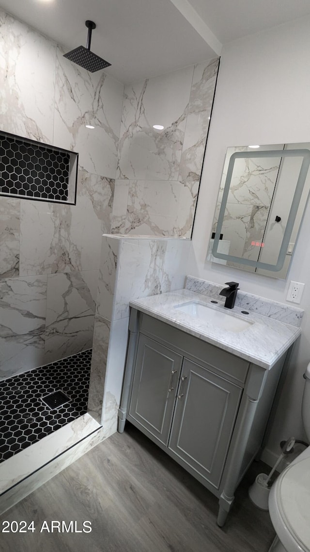 bathroom featuring tiled shower, vanity, wood-type flooring, and toilet