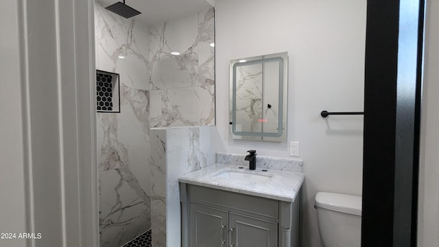 bathroom with a tile shower, vanity, and toilet