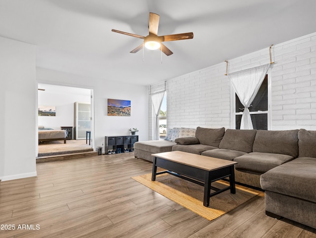 living room featuring light hardwood / wood-style floors, ceiling fan, and brick wall