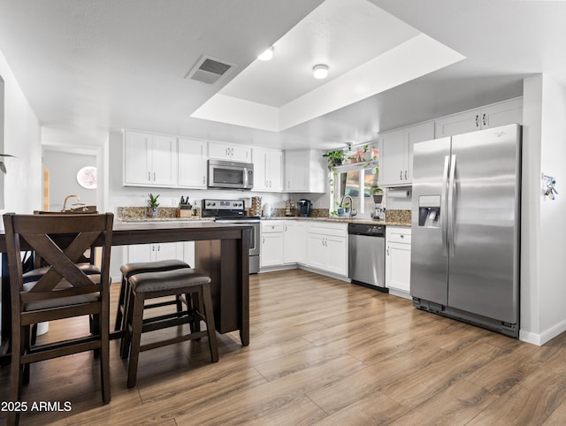 kitchen with white cabinetry, sink, a tray ceiling, stainless steel appliances, and light hardwood / wood-style flooring