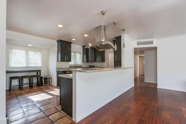 kitchen with sink, hanging light fixtures, kitchen peninsula, island exhaust hood, and light stone countertops