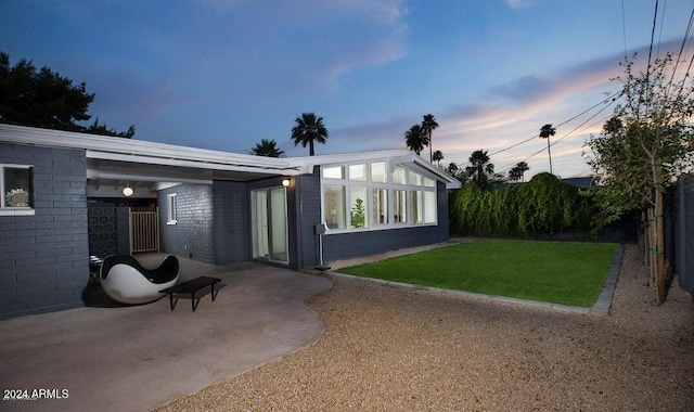 back house at dusk with a patio area and a yard