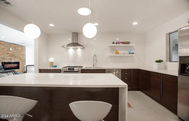 kitchen featuring stainless steel appliances, dark brown cabinetry, sink, decorative light fixtures, and wall chimney range hood