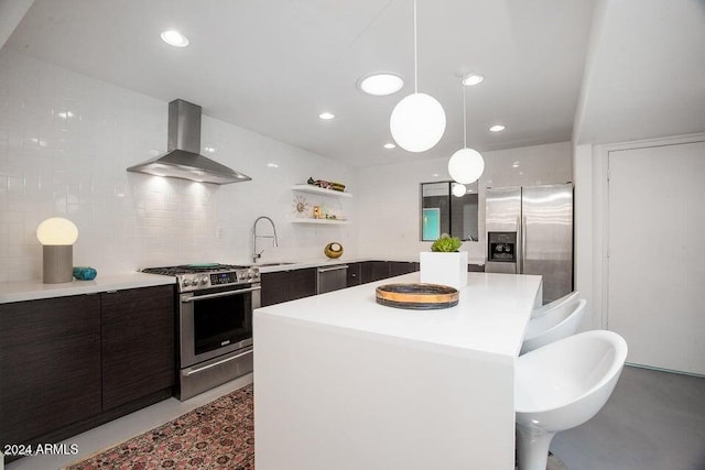 kitchen featuring a center island, sink, wall chimney range hood, appliances with stainless steel finishes, and decorative light fixtures