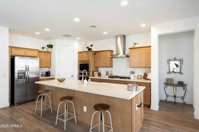 kitchen with a center island with sink, wall chimney exhaust hood, stainless steel appliances, and a breakfast bar area