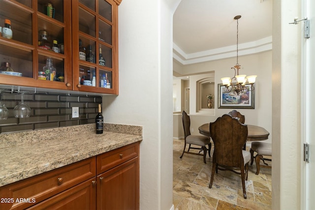 bar with decorative light fixtures, an inviting chandelier, light stone counters, and tasteful backsplash