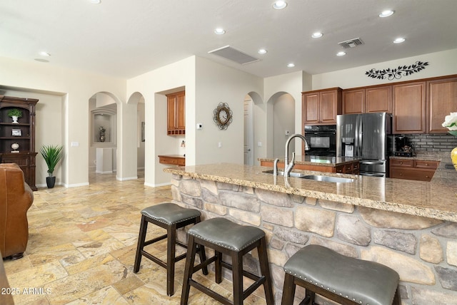 kitchen with oven, light stone counters, a kitchen bar, decorative backsplash, and stainless steel fridge with ice dispenser