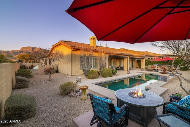 back house at dusk featuring an outdoor fire pit, a patio area, a fenced in pool, and a mountain view