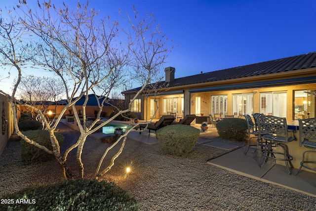 back house at dusk featuring a pool, a patio, and an outdoor hangout area