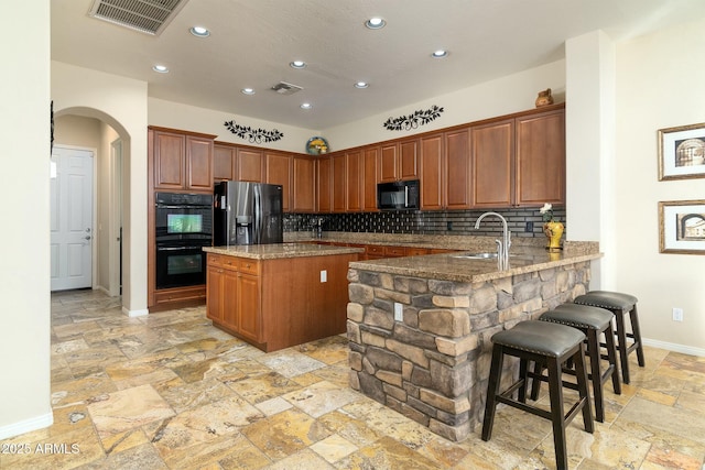 kitchen featuring black appliances, light stone countertops, kitchen peninsula, a breakfast bar, and tasteful backsplash