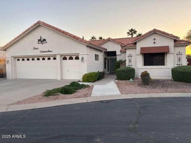 mediterranean / spanish home with a garage, driveway, stucco siding, and a tiled roof