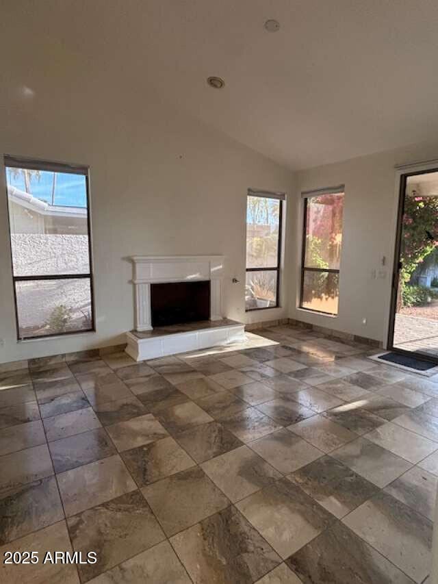 unfurnished living room featuring lofted ceiling, a fireplace with raised hearth, and baseboards