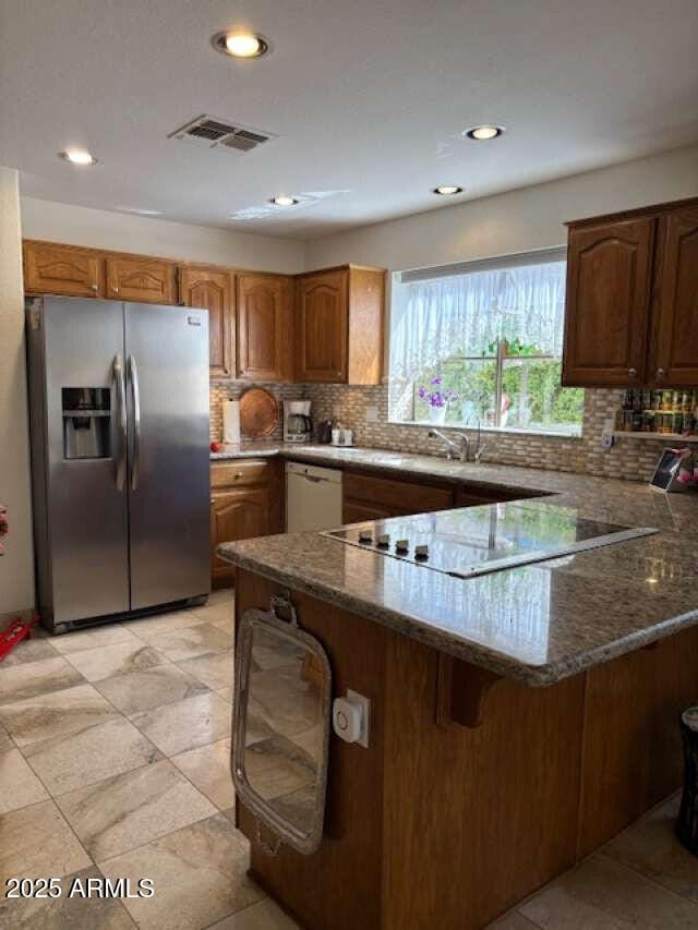 kitchen with stainless steel fridge with ice dispenser, a peninsula, dark stone countertops, decorative backsplash, and recessed lighting