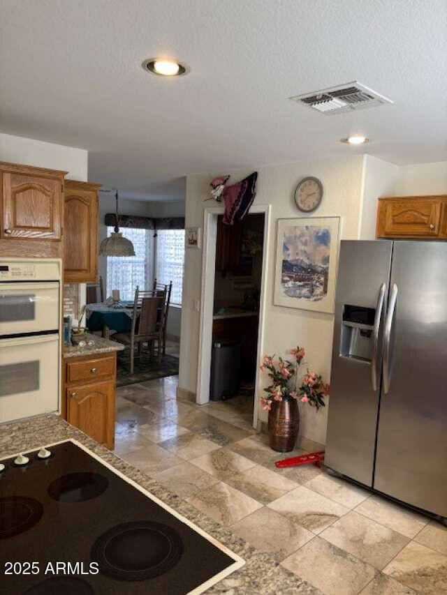 kitchen with stainless steel refrigerator with ice dispenser, white double oven, black electric stovetop, brown cabinetry, and a textured ceiling