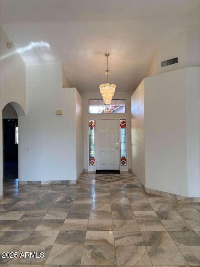 entrance foyer featuring arched walkways, a towering ceiling, a chandelier, and baseboards