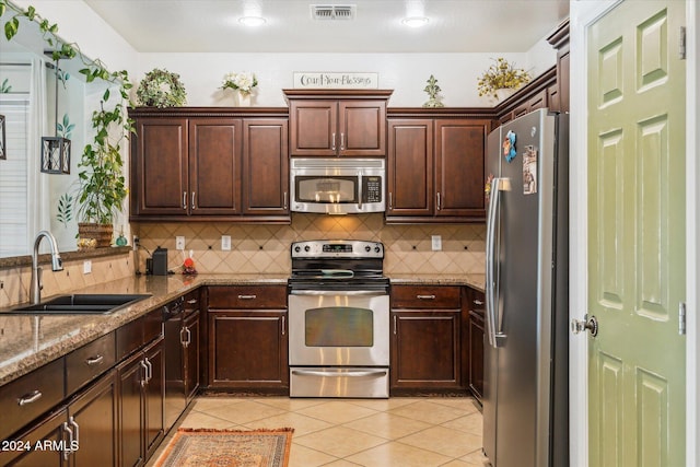 kitchen with sink, tasteful backsplash, light stone counters, dark brown cabinetry, and stainless steel appliances