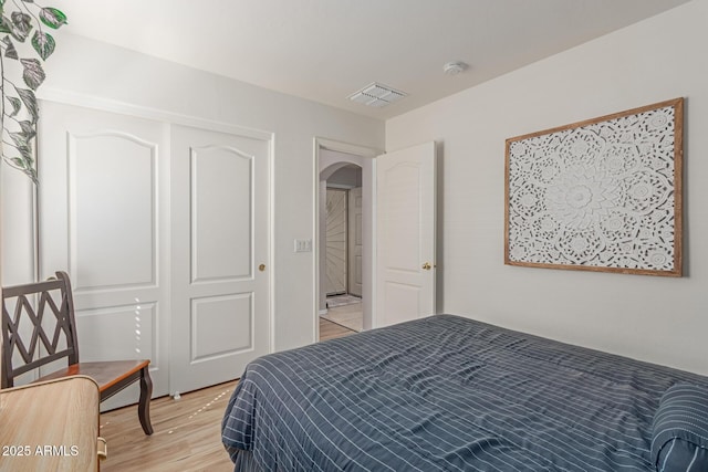 bedroom featuring arched walkways, light wood finished floors, and visible vents