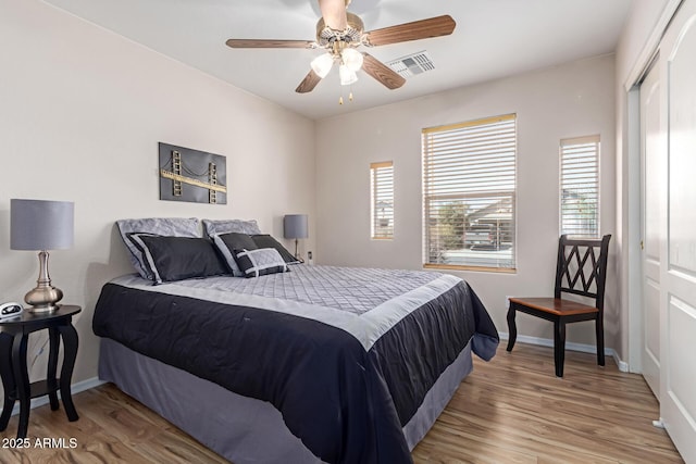 bedroom with baseboards, visible vents, a ceiling fan, wood finished floors, and a closet