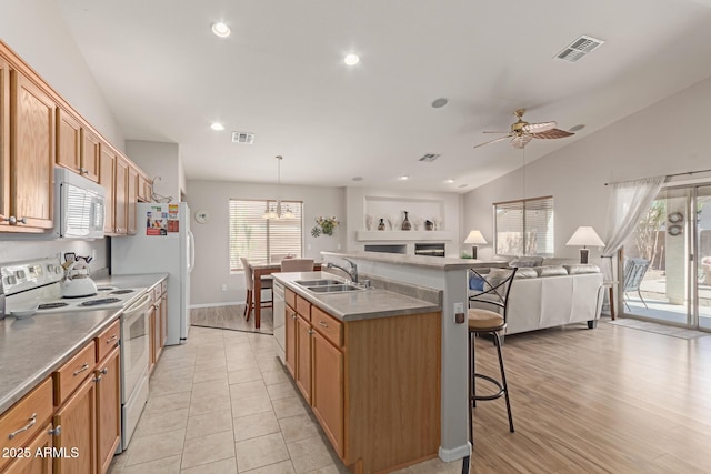 kitchen featuring white appliances, a sink, a kitchen breakfast bar, vaulted ceiling, and an island with sink