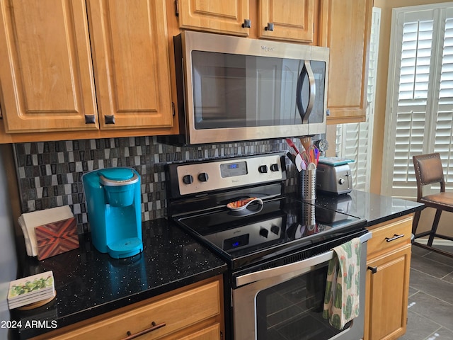 kitchen featuring light tile floors, appliances with stainless steel finishes, dark stone counters, and tasteful backsplash