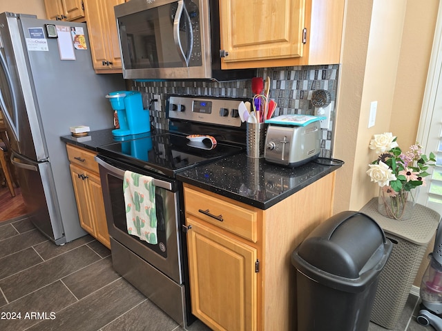 kitchen with backsplash, dark tile floors, stainless steel appliances, and dark stone countertops