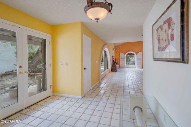 corridor with light tile patterned flooring, french doors, a textured ceiling, and vaulted ceiling