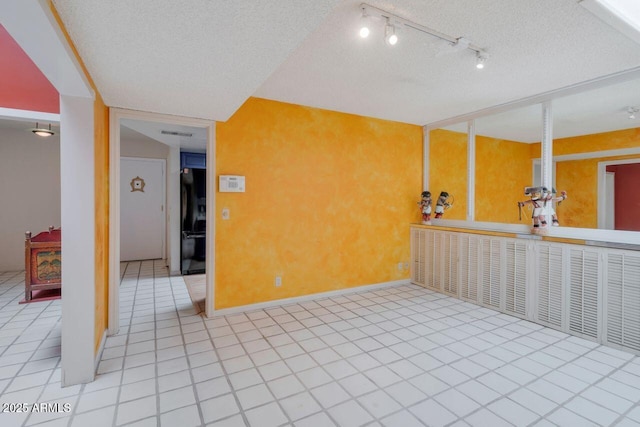 tiled empty room with rail lighting, baseboards, visible vents, and a textured ceiling