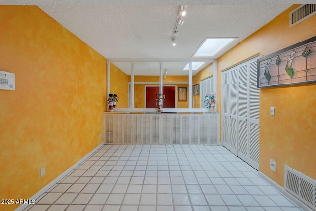 spare room with tile patterned floors, rail lighting, visible vents, and a textured ceiling